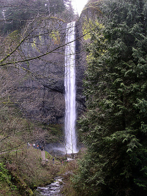 [A very long, thin drop of water beyond the rocks and landing in a pool before dripping down to lower levels.]